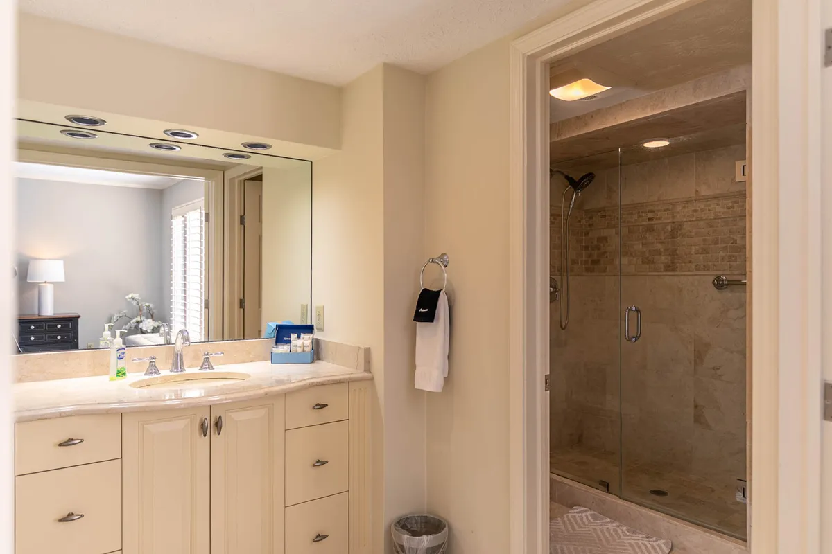 A modern, calming bathroom is displayed, featuring a double vanity sink, a large mirror that enhances the sense of space, and a contemporary shower area. The atmosphere is serene and spa-like, with plush towels and soft lighting.