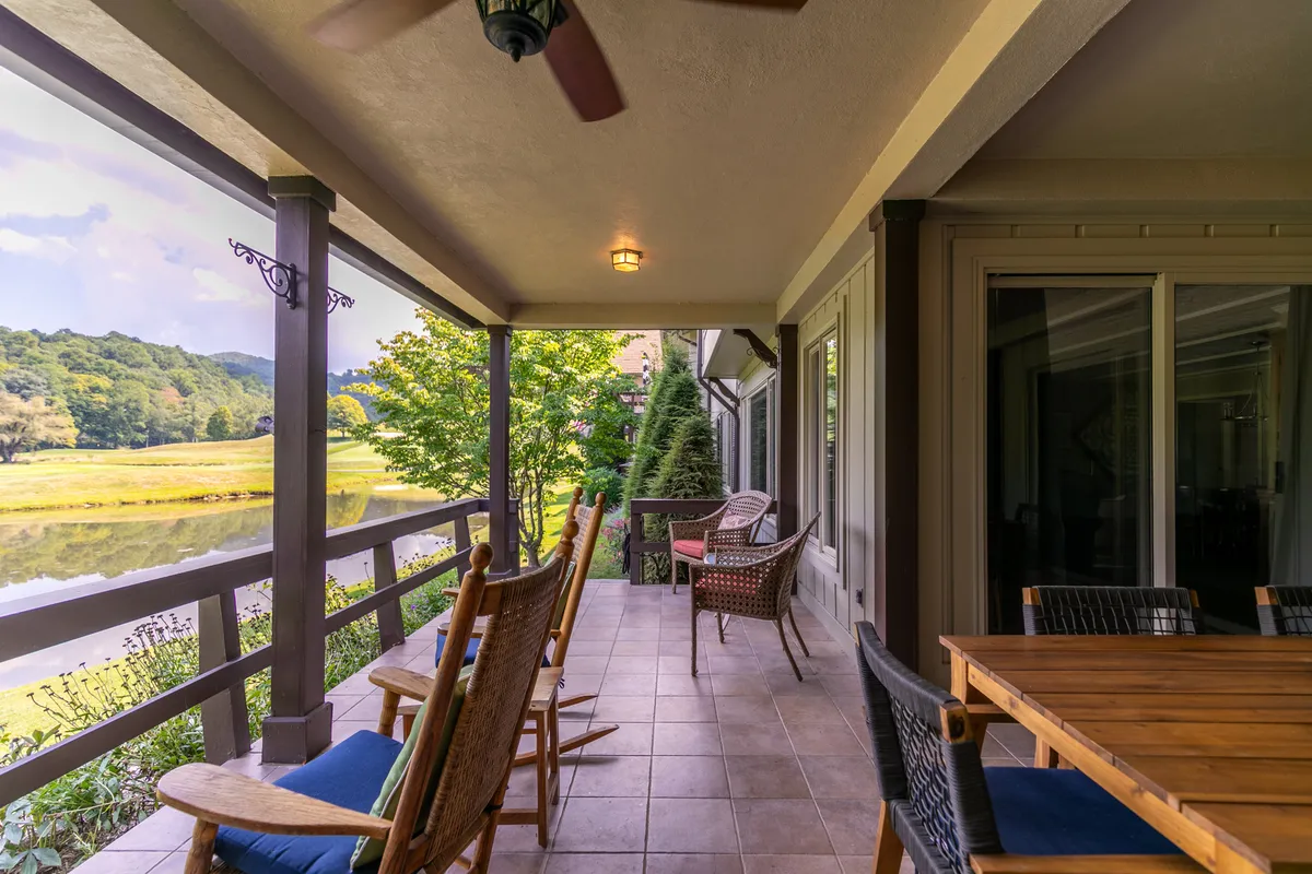 A tranquil porch setting with rocking chairs and a wooden table, looking out over lush landscaping and distant views. Potted plants add a homey touch, and the space looks inviting for morning coffee, quiet reading, or relaxed conversations.