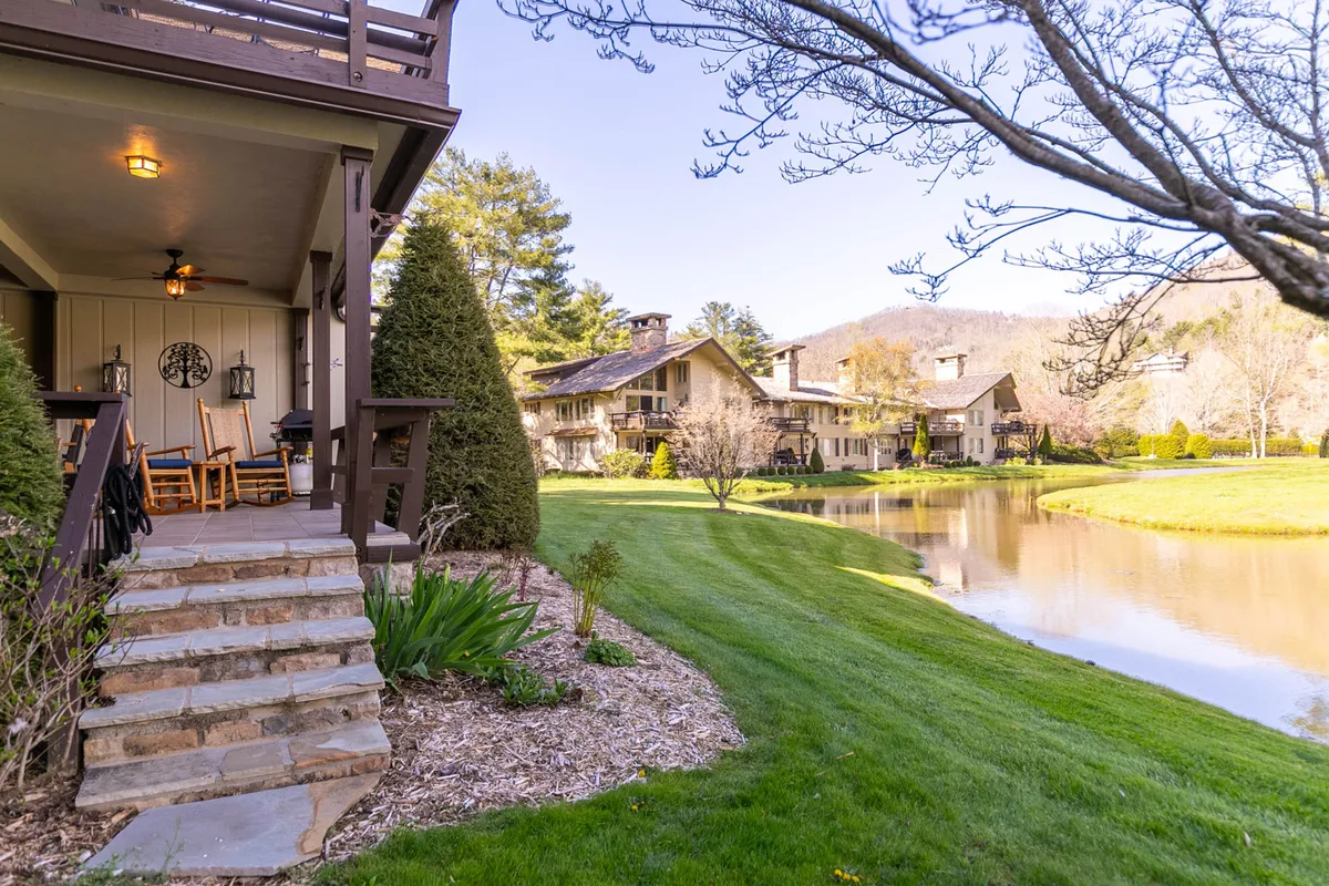 Steps lead up to a welcoming porch surrounded by a green lawn, pond, and mature trees. The porch offers a vantage point for enjoying sunrise views and observing wildlife, while the overall vibe is peaceful and exclusive.