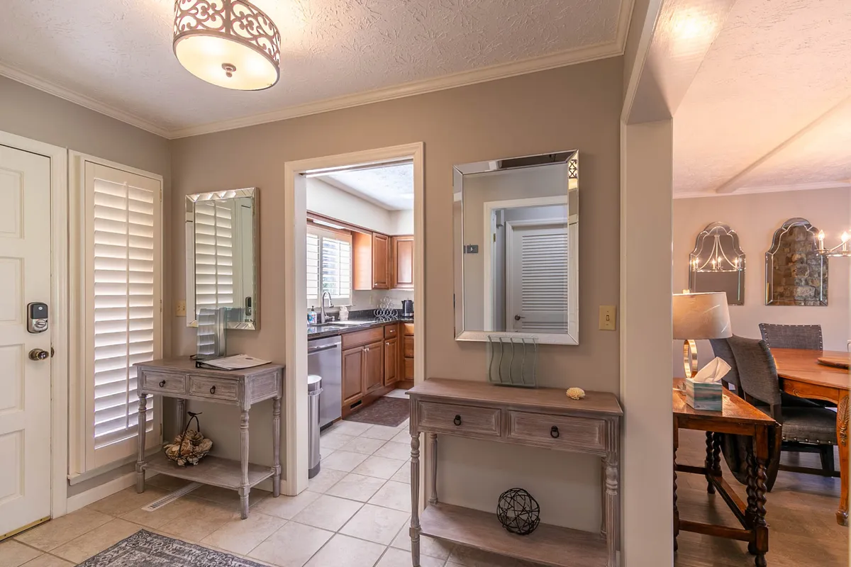A welcoming interior shot showing the entrance door leading into a hallway with mirrors and a console table. The image also offers a glimpse into the kitchen and dining area beyond, highlighting the open flow and easy access between spaces.