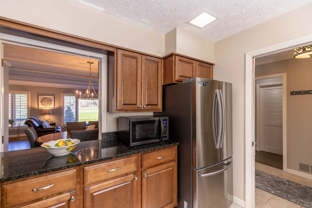 A stylish kitchen setting with dark wooden cabinets, a stainless steel refrigerator, and a contrasting black granite countertop. A fruit bowl adds a homey touch, while the spaciousness and layout encourage both cooking and entertaining.